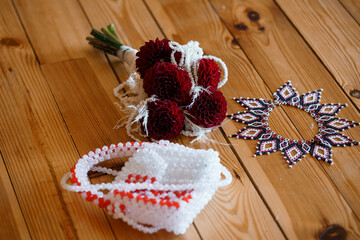 Traditional Ukrainian Wedding Accessories: Red and White Floral Bouquets, Beadwork Korovai and Vyshyvanka Elements on Wooden Table Texture.