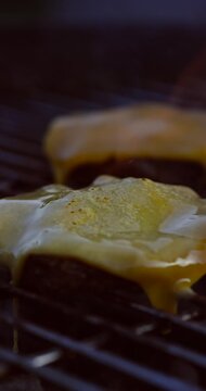 Close-up of melting cheese on grilled beef patty with smoke and heat rising, delicious BBQ moment.