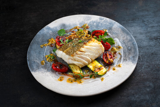 Fried skrei cod white sea fish filet with green vegetable and tomato, rice passion fruit relish umami sauce  Mediterranean dish recipe