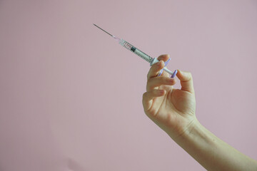 gloved hand holding multiple colorful syringes, against a soft background. Conceptual image related...