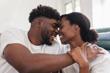 Affectionate African American couple sitting close together indoors, touching foreheads and smiling lovingly, expressing warmth, tenderness, emotional connection, and a happy romantic relationship