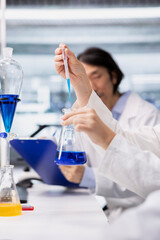 Close up of microbiologists brainstorming, using pipette to dispense reagent into test tube at laboratory bench. Modern research facility coworkers do pipetting procedure with dropper