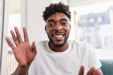 Smiling man having a videocall at home, talking and gesturing expressively while wearing a casual white t-shirt. Bright natural light and relaxed atmosphere convey friendliness and confidence