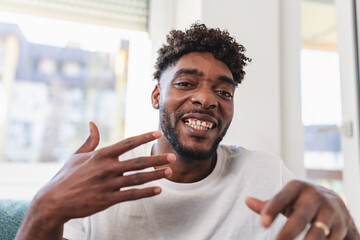 Smiling man having a videocall at home, talking and gesturing expressively while wearing a casual white t-shirt. Bright natural light and relaxed atmosphere convey friendliness and confidence