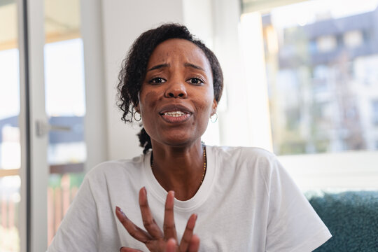 Young African American woman sitting indoors during a video call with a friend or family member, smiling warmly and reacting emotionally in a relaxed home environment