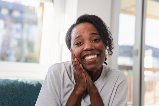 Young African American woman sitting indoors during a video call with a friend or family member, smiling warmly and reacting emotionally in a relaxed home environment