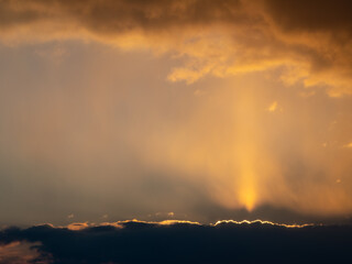 Dramatic golden sunset with radiant light beams breaking through dark storm clouds, creating a peaceful yet powerful sky scene