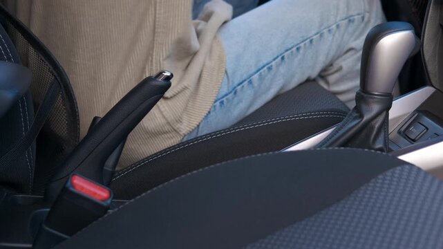 Woman fastening seat belt and shifting gears in car. Woman driver fastening seat belt, holding gear shift lever inside car, preparing to drive and ensure road safety