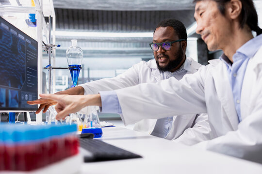 Team of biochemists in laboratory pointing to computer display, doing DNA data analysis. Research facility colleagues doing brainstorming using bioinformatics genomics software on PC in high tech lab