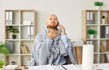Young sick man suffering from a sore throat sitting on workplace in office and talking by mobile...