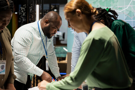 Coworkers prepare for a presentation by reviewing documents inside the strategy room at night, exchanging reports files and delivering forecasting updates for enterprise management. - Powered by Adobe