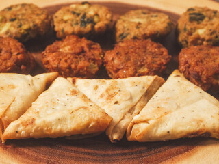Close up of Indian style starter food selection of samosa, bhajis and pakoras on wooden board. Party sharing finger food variety made from fine products and aromatic spices. Special orient vibe.