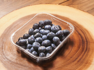 A plastic tray of blueberries sits on a wooden table. The tray is clear and filled with fresh organic fruits ready for consumption. Healthy diet concept. Natural product.