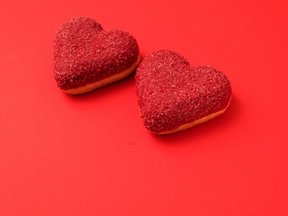 Obraz premium Two heart shaped doughnuts on red color surface. Top of the product is covered with colored sweet icing. Food for a Valentine day or special romantic event. Creative bakery product.