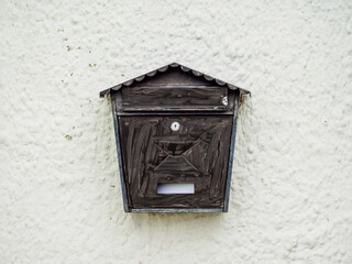 A metal mailbox with opening to see incoming mail mounted on a white wall of a residential building. The mailbox is old and has a rustic appearance