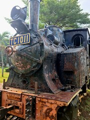 Old steam locomotive from Dutch colonial era displayed outdoors. Vintage train engine showing rusted metal texture
