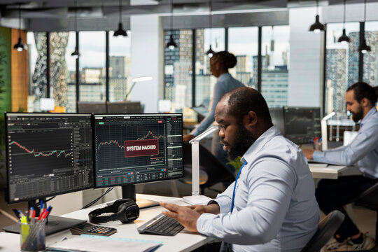 Prop firm trader seeing warning popup of hacking activity, working to secure account. African american man reacting to stock market account perpetrated by hackers looking to gain trade secrets