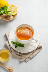 Hot tea with lemon, ginger, honey, and mint in a cup on a light background with citrus fruits