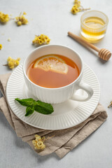 Hot tea with lemon, honey, and mint in a cup on a light background with dry flowers close up.