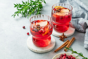 A cranberry drink in a two glasses on a light background with cinnamon, berries and green branch.