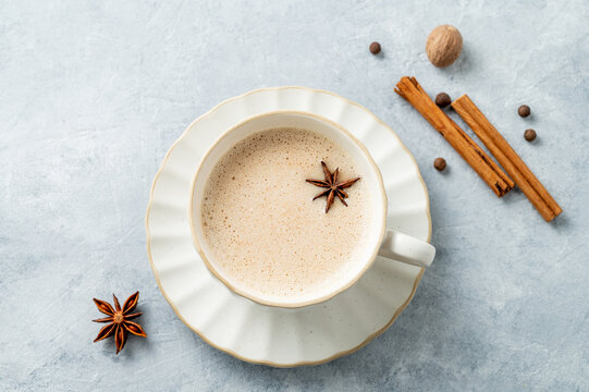 Traditional Indian masala chai tea with milk and spices in a white cup on a light background close up.