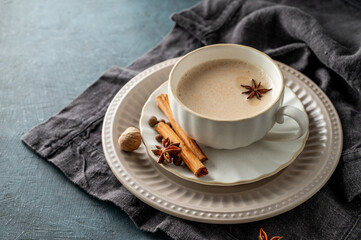 Traditional Indian masala chai tea with milk and spices in a white cup on a plate on a dark...