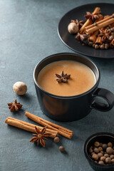 Traditional Indian masala chai tea with milk and spices in a black cup on a dark background.