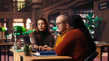 Multiethnic group of students discussing about academic materials, reading and doing research for upcoming exams. Diverse people showing commitment for personal growth.