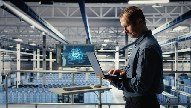 Technician monitors server room activity using laptop while walking through facility. Data center IT professional reviews rigs tests results to ensure systems are working correctly, camera A - Powered by Adobe
