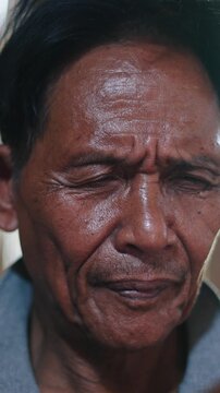 Close-up face and hands of Asian senior man focused on smartphone use inside a traditional lahu house in asia