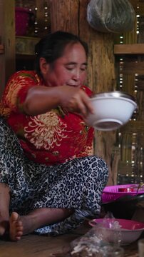 Southeast Asian woman carefully preparing a home-cooked meal inside a traditional rural kitchen with rustic bamboo walls