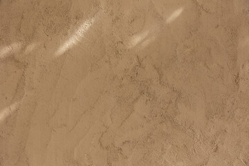 Close-up of a beige plaster wall texture illuminated by soft natural light and subtle shadows....