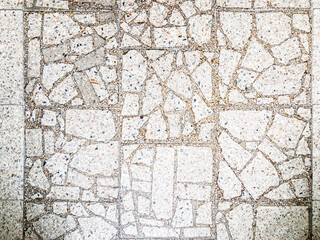 Close-up of a textured, gray, cracked and lined tile floor with an interlocking mosaic pattern Depth is suggested by varying sizes and shapes, possibly creating relief or 3D quality Light comes fro