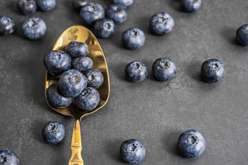 Close-up of perfect blueberries on a black leather background with a nickel silver spoon highlighting the purple tones of the fruit