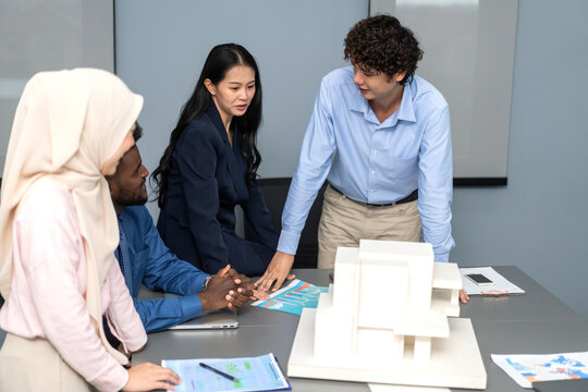 Architects engineers collaborating on building design project in modern office, diverse team of professionals female muslim architect and male engineers discussing architectural model of structure