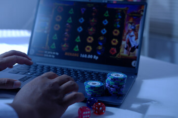 Close-up of a man's hands playing online slot gambling in front of a laptop with a stack of dice and poker chips, ready to express his victory. The concept of gambling. Winning and losing in gambling.