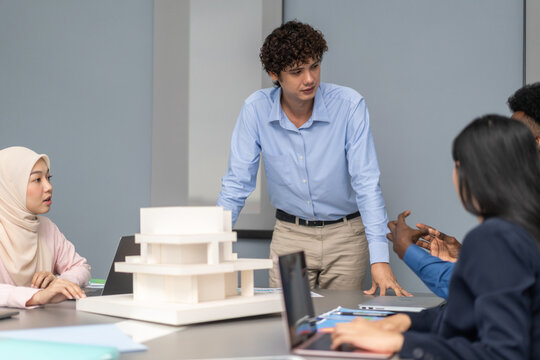 Architects engineers collaborating on building design project in modern office, diverse team of professionals female muslim architect and male engineers discussing architectural model of structure