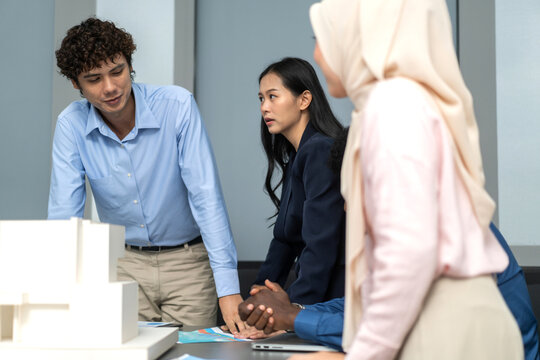 Architects engineers collaborating on building design project in modern office, diverse team of professionals female muslim architect and male engineers discussing architectural model of structure - Powered by Adobe