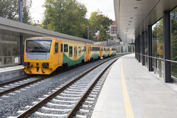 Fototapeta premium Yellow and green commuter train is parked at a modern station platform, surrounded by trees and contemporary architecture, showcasing urban transportation infrastructure