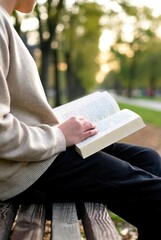 Person reading book on park bench in soft sunlight, calm minimalist lifestyle scene
