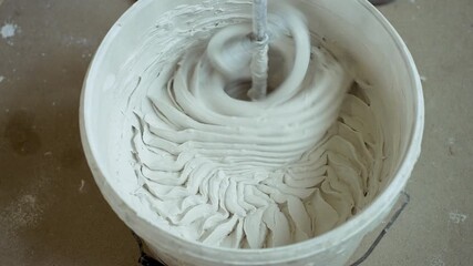Construction process. Putty diluted with water in bucket is mixed with power tool, mixer. Process of mixing putty for wall finishing, applying it to surface. Close-up of professional builder at work.