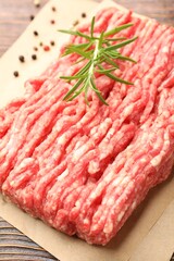 Raw minced meat with peppercorns and rosemary on wooden table, closeup