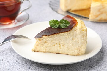 Piece of delicious Basque cheesecake with mint and tea on light grey table, closeup