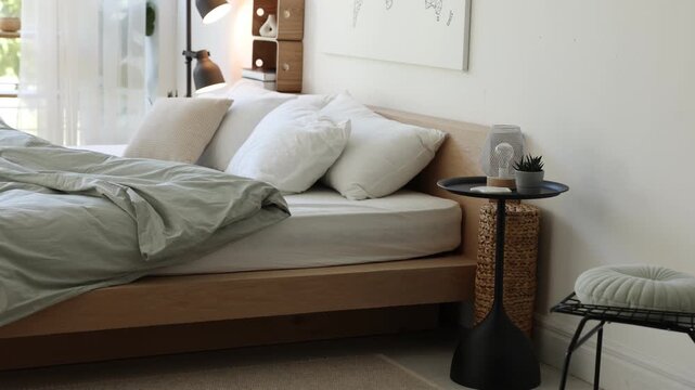 Cozy large bed, side table and lamp near white wall in bedroom, camera moving down
