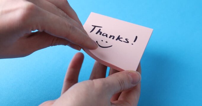 Woman taking note with word Thanks on light blue background, closeup