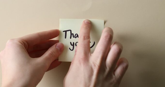 Woman putting note with words Thank You onto cork board, closeup