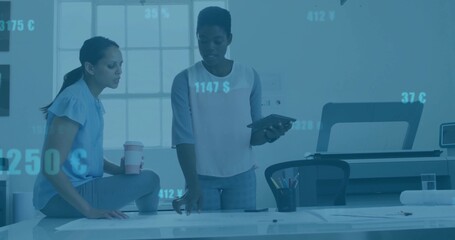 Collaborating colleagues examining plans on drafting table in design studio, with tablet and coffee