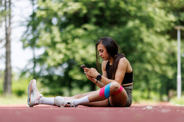 Young Woman Sitting On Track Checking Her Smartphone During Outdoor Exercise