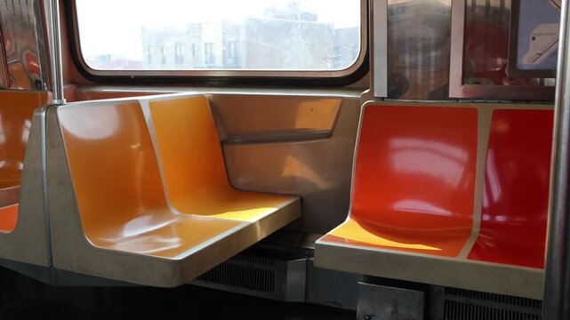 empty seats and looking out the window of moving elevated subway train in new york city nyc brooklyn metro commute pov move ride riding nobody yellow orange red seats d line passing buildings