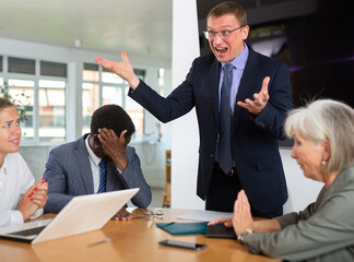 Angry businessman manager boss shouting at group office meeting scolding employees mad about...